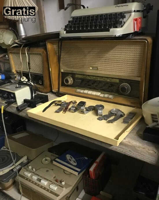 alte Schreibmaschinen und historische Radios. Uhren, meist mit Metallbändern und -gehäusen, in einer Ablage davor. 